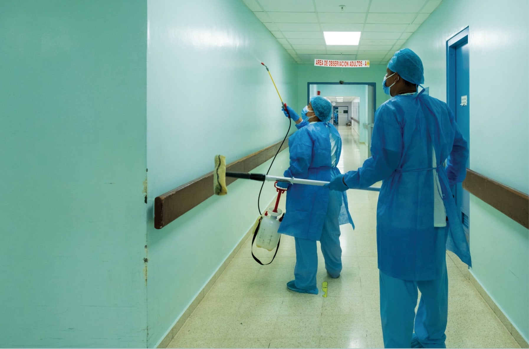 Two healthcare workers in protective gear disinfecting a hospital corridor.