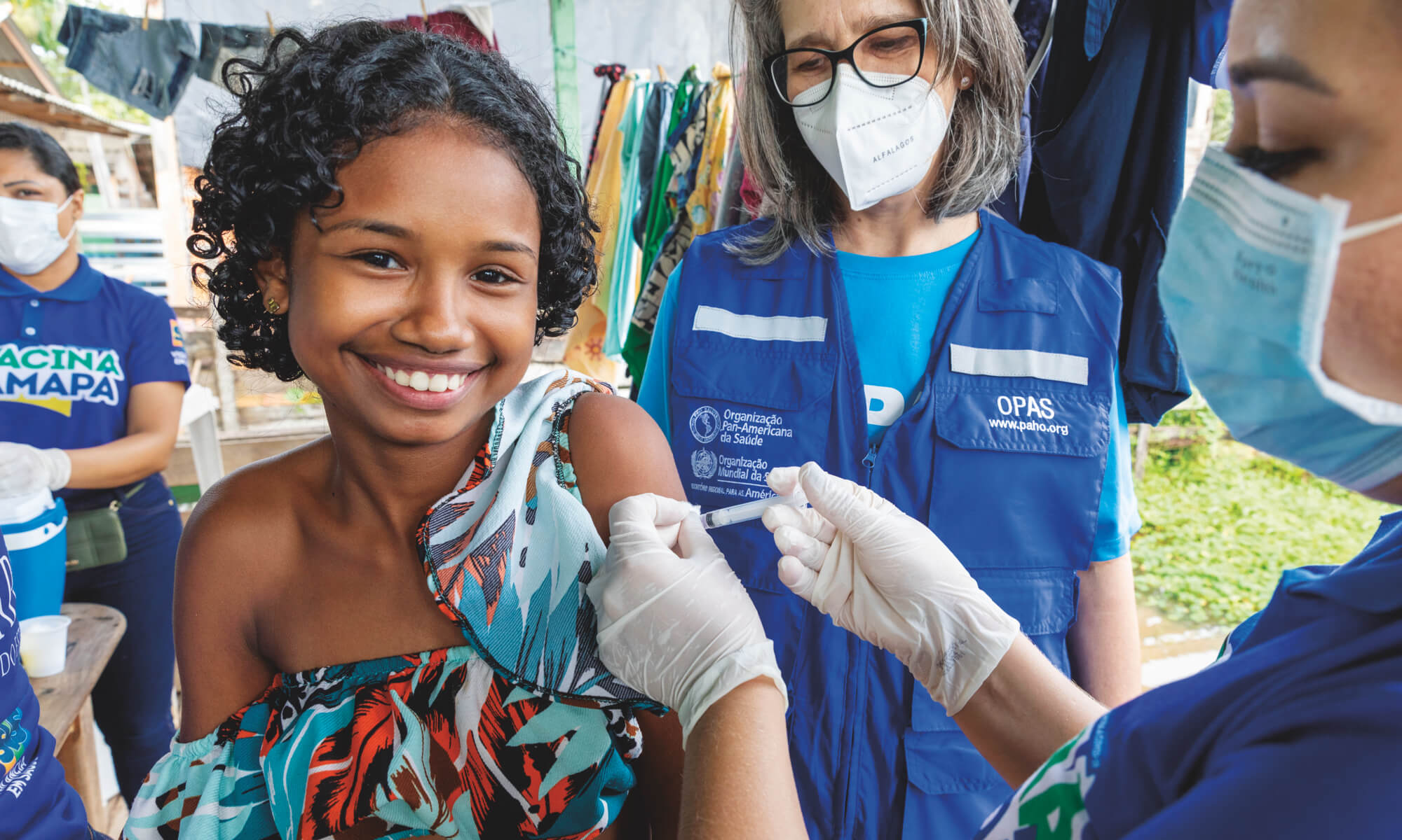 A young girl smiles while receiving a vaccine shot from a healthcare worker.