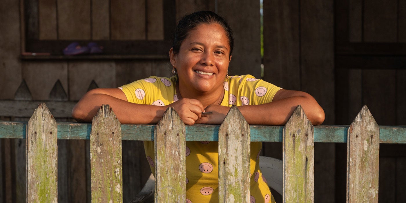 Woman from the Americas smiling while resting on a picket fence