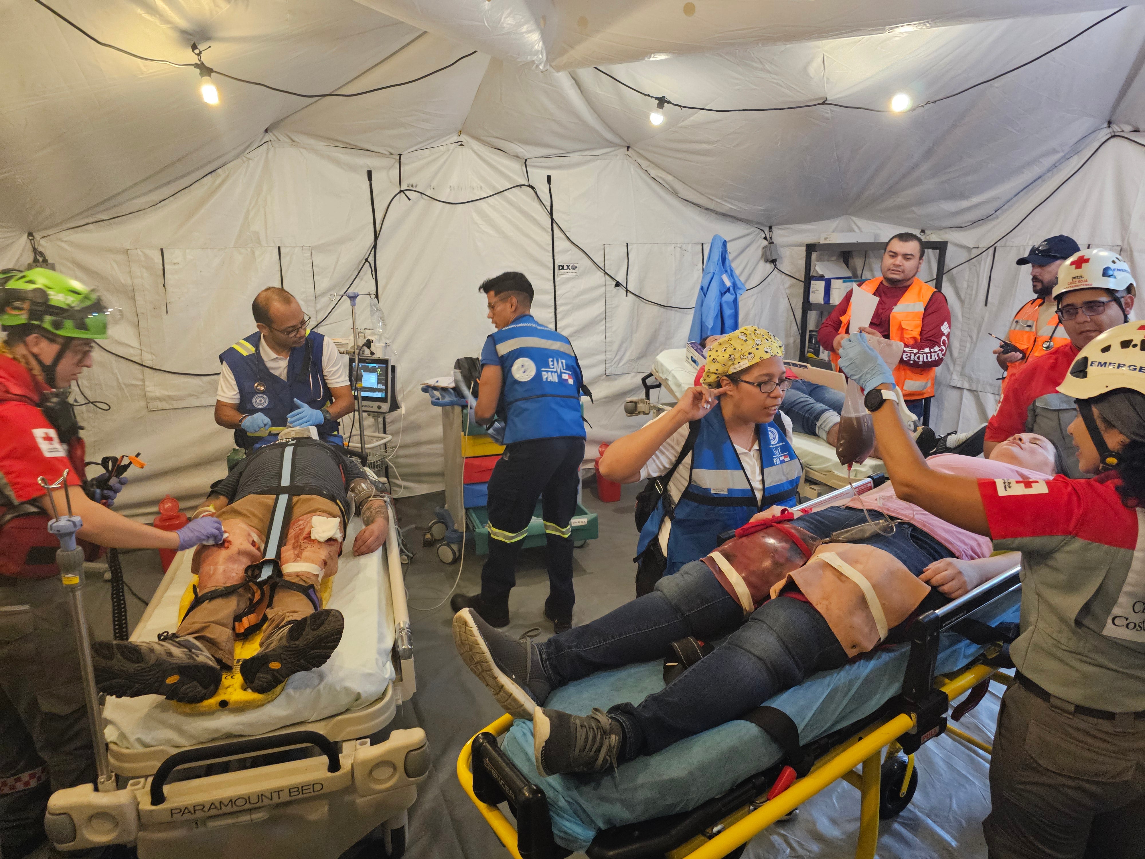 personal de respuesta a emergencias de salud junto a pacientes en camilla dentro de una carpa