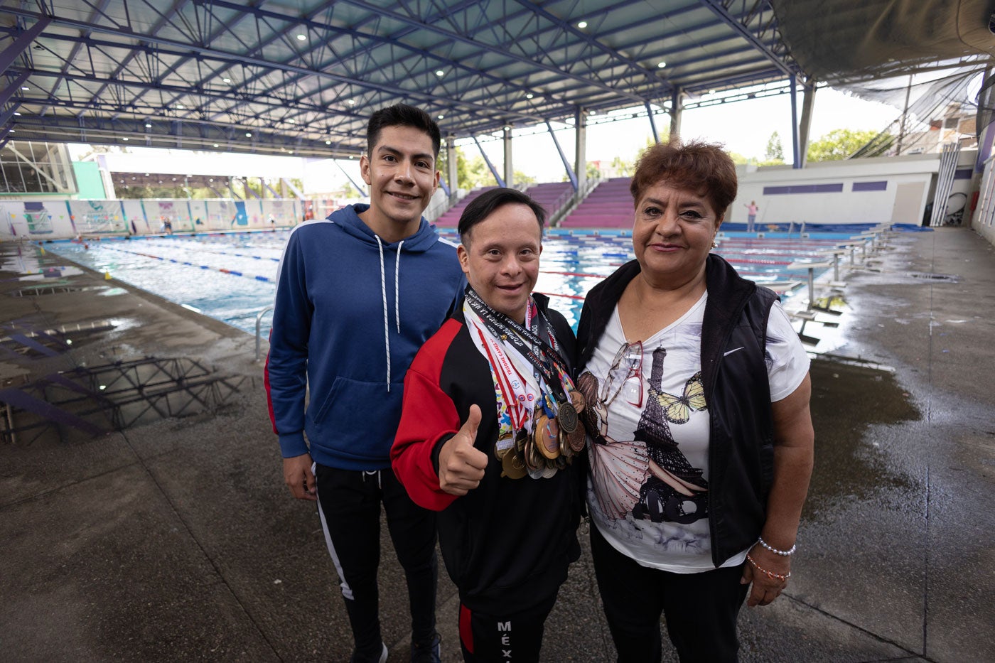 Giovanni Flores muestra las medallas que ha ganado nadando. Posa con un chico y su madre.