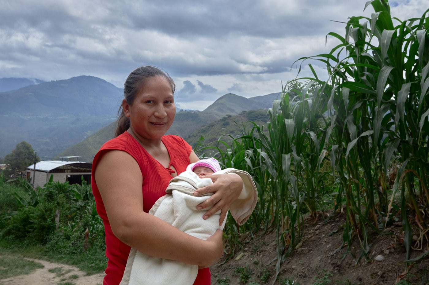 Mother with newborn stand outdoors with mountains in the background