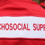 Photo of the back of a healthcare worker dressed with a red jacket with the sign "Psychosocial support" in red typography over white background. Only part of the back is seen, from the top of the shoulders to the mid part of the back