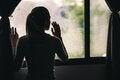 Silouette of a girl looking out of a window, in the shadows