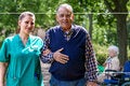 older man and nurse walking in wooded area with an older women in a wheelchair in the background