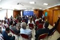 Foto del salón desde atrás. Se ven las personas sentadas y, al fondo, la mesa con autoridades.