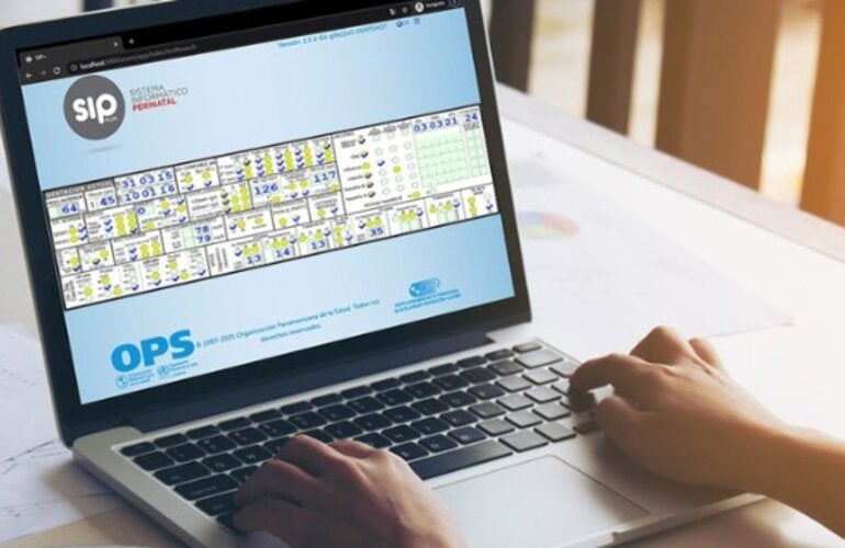 Computadora sobre un escritorio. En la pantalla se ve el Sistema de Información Perinatal. Hay unas manos sobre el teclado.
