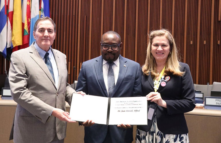 Jean-Patrick Alfred holds the PAHO Award for Management and Leadership. He is standing next to the PAHO Director and the Directing Council president.