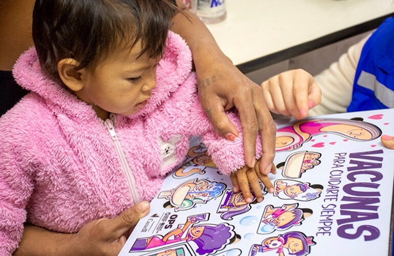 Foto de niña con su mamá a la espera de ser vacuna mientras juega con un rompecabezas sobre vacunas