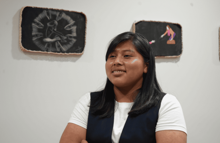 Adolescente indígena posando frente a sus obras de arte exhibidas