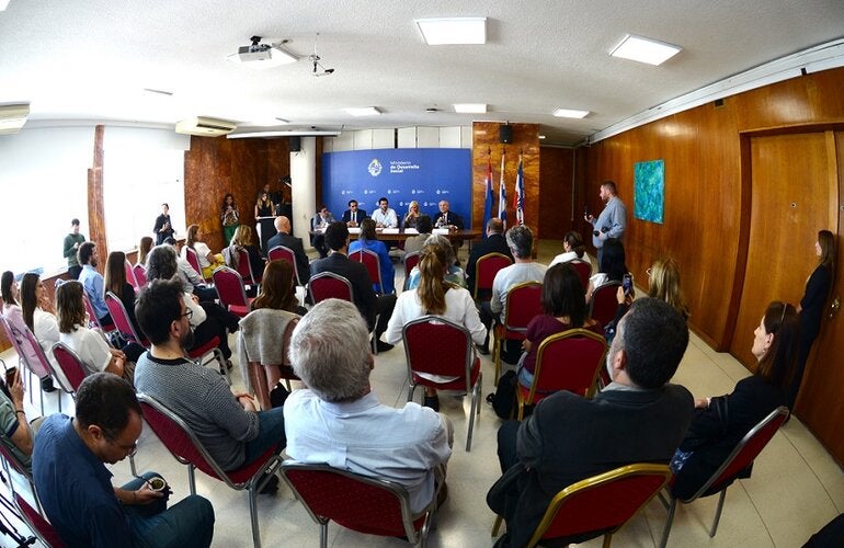 Foto del salón desde atrás. Se ven las personas sentadas y, al fondo, la mesa con autoridades.