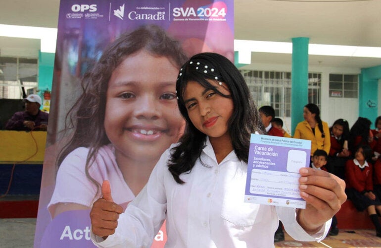 Girl poses with vaccination booklet in hand after receiving vaccine