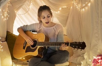 Girl playing a guitar under a tent made of cloth illuminated by a string of ligths