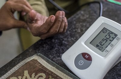 Close up of a glucometer and in the back a hand holding the hand of a patient