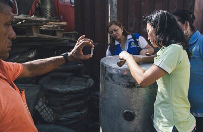 Control over breeding focus: Health workers review and find mosquito larvae in standing water within one of the containers at an enclosure of tires and useless iron containers.