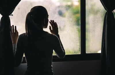 Silouette of a girl looking out of a window, in the shadows