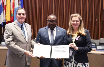 Jean-Patrick Alfred holds the PAHO Award for Management and Leadership. He is standing next to the PAHO Director and the Directing Council president.