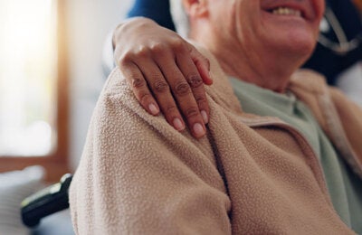 Older man in wheelchair is embraced by caregiver