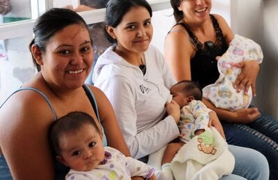 mujeres sentadas, mirando a cámara y sonriendo, con sus hijos bebés en brazos