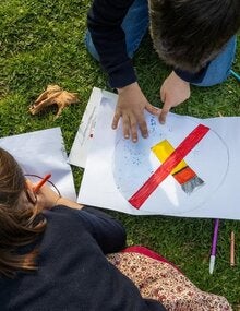 Two young children drawing anti tobacco signs over a grassy floor, surrounded by pens and pencils of may colors