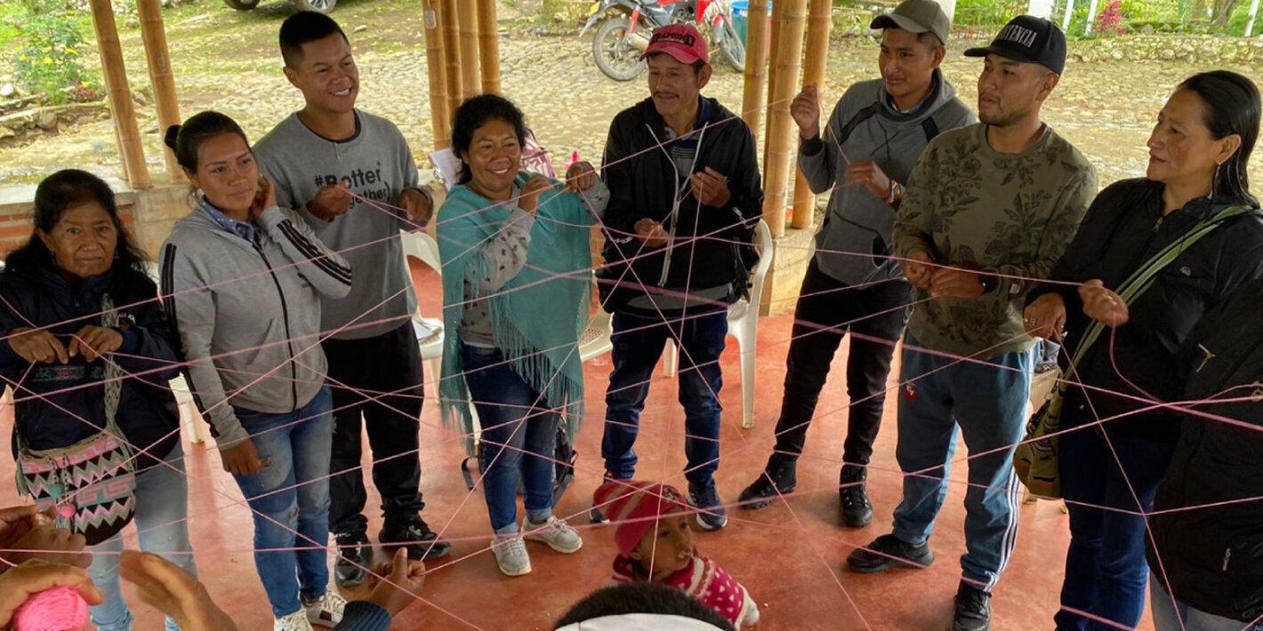Indigenous people forming a circle and grabing a thin red interconected rope