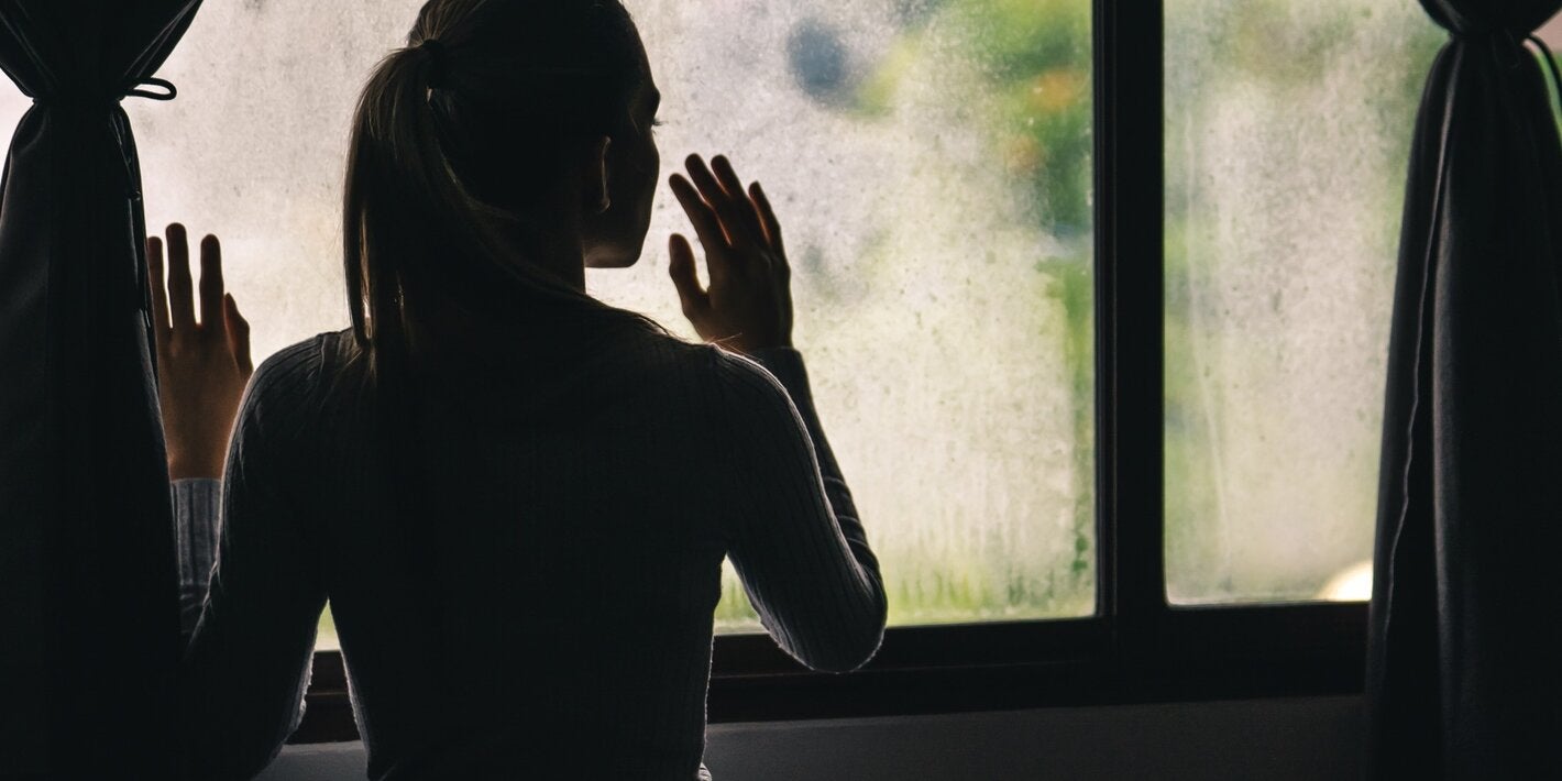 Silouette of a girl looking out of a window, in the shadows