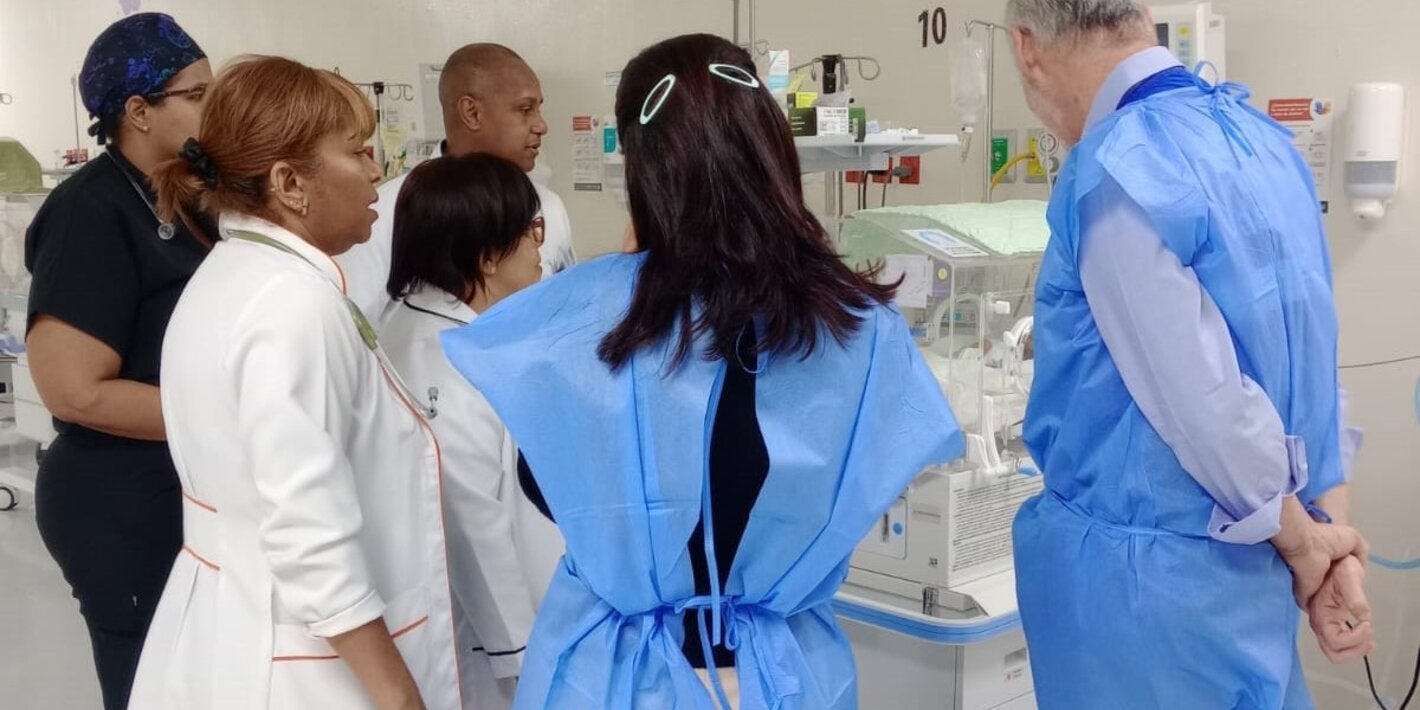 Profesionales de la salud y de OPS alrededor de una incubadora observando a un recién nacido.