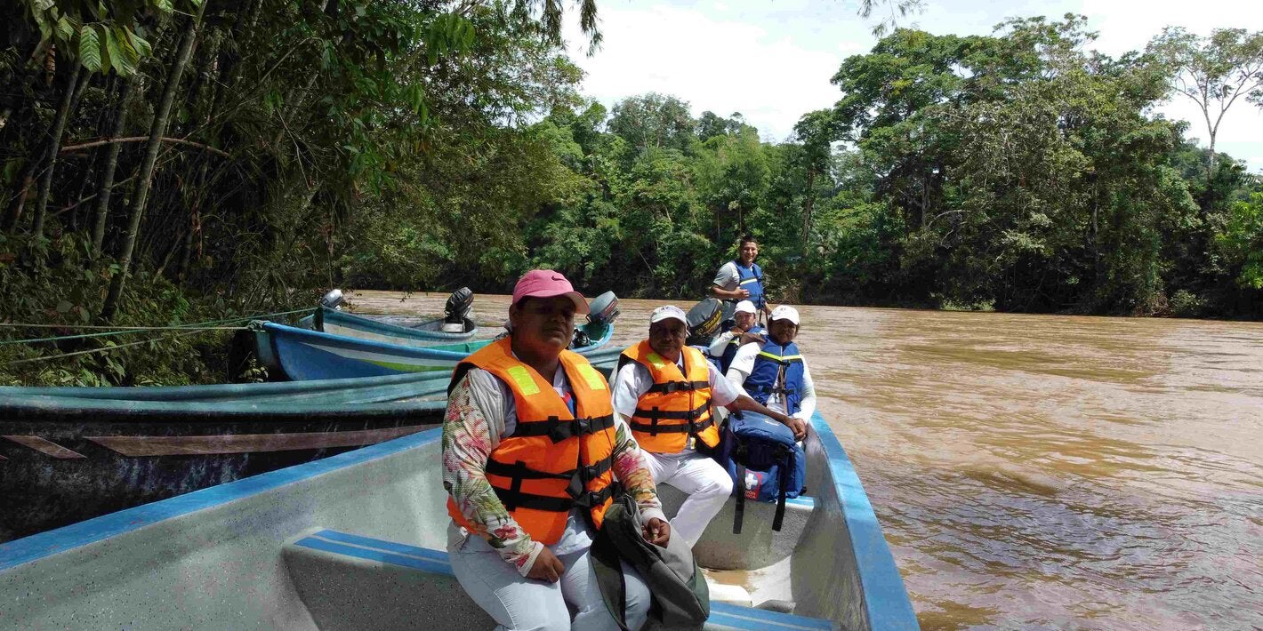 Personas en un bote de madera en la orilla de un río. Las personas tienen chalecos salvavidas.