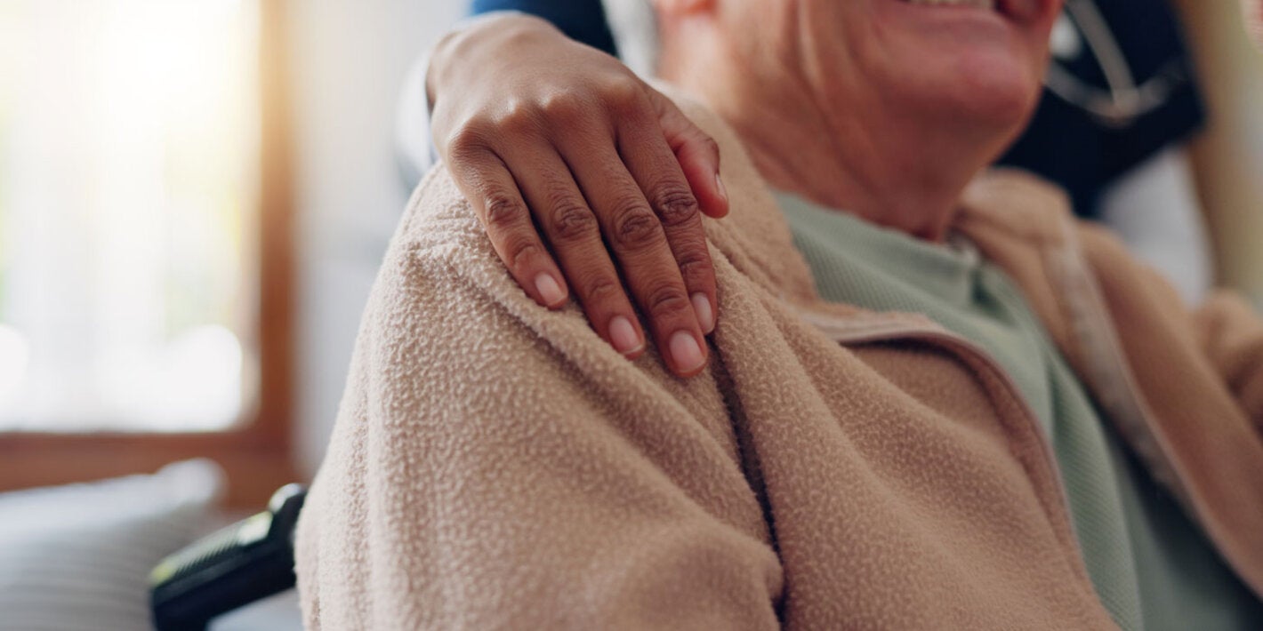 Older man in wheelchair is embraced by caregiver