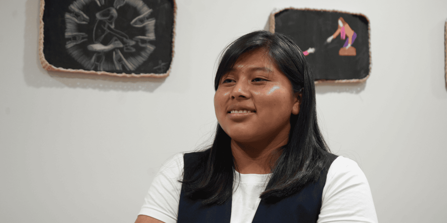 Adolescente indígena posando frente a sus obras de arte exhibidas