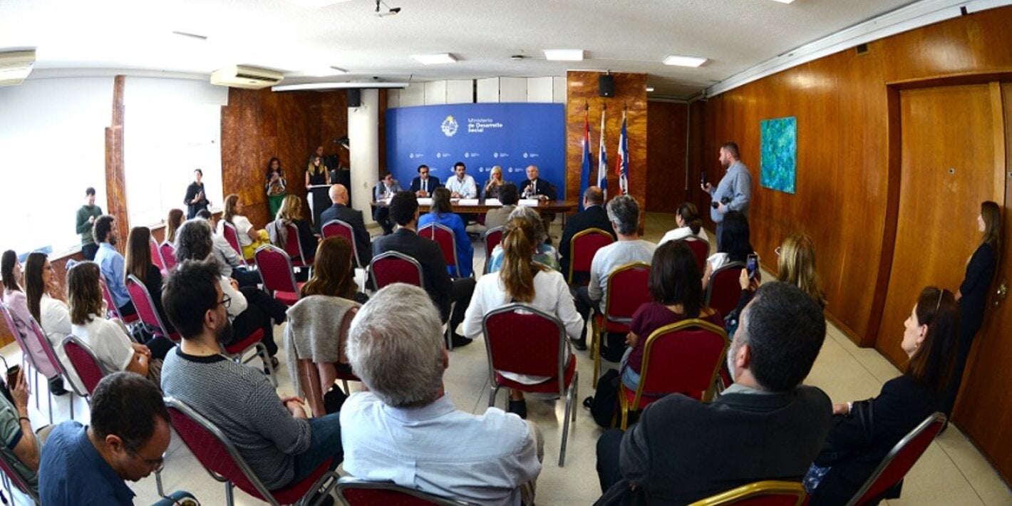 Foto del salón desde atrás. Se ven las personas sentadas y, al fondo, la mesa con autoridades.