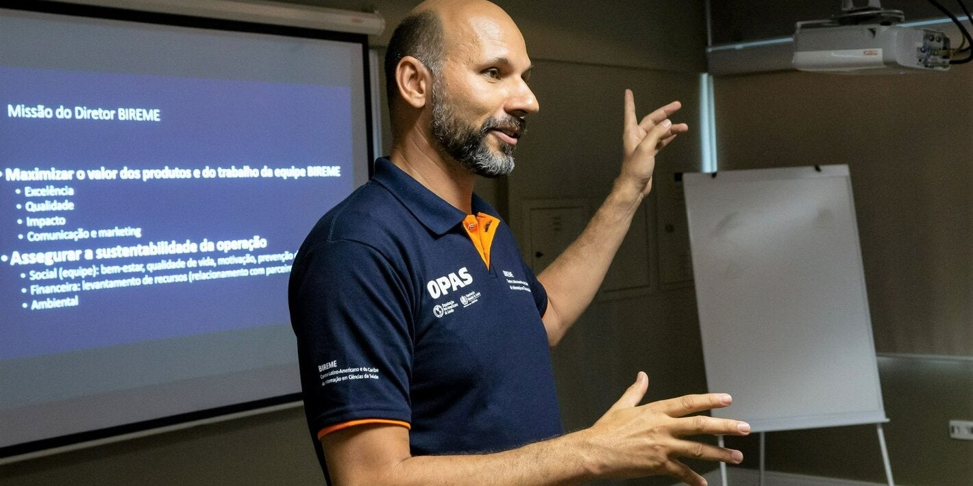 A photo of João Paulo Souza, Director of BIREME, wearing a PAHO shirt, speaking and gesturing at a lecture.