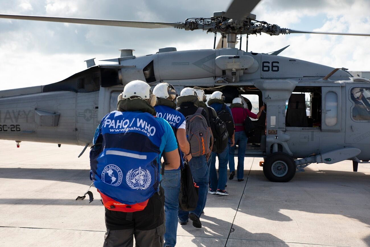 emergency medical team wearing blue vests with PAHO/WHO logo and white helmets, heading to a helicopter