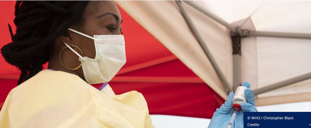 Woman - healthcare worker, wearing a facemask and protective gown, preparing an injectable vaccine to be administrated