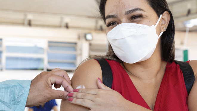 Woman - healthcare worker, wearing a facemask and protective gown, preparing an injectable vaccine to be administrated