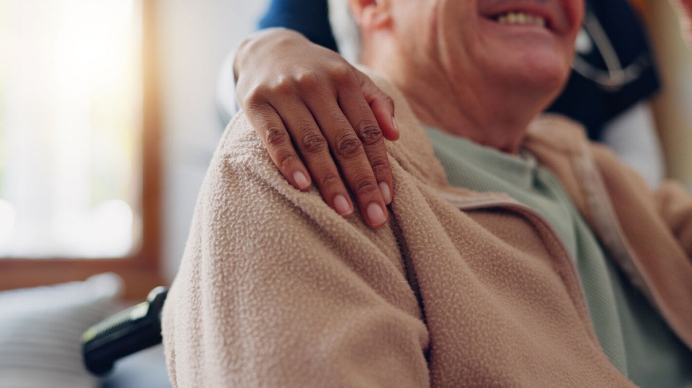 Older man in wheelchair is embraced by caregiver