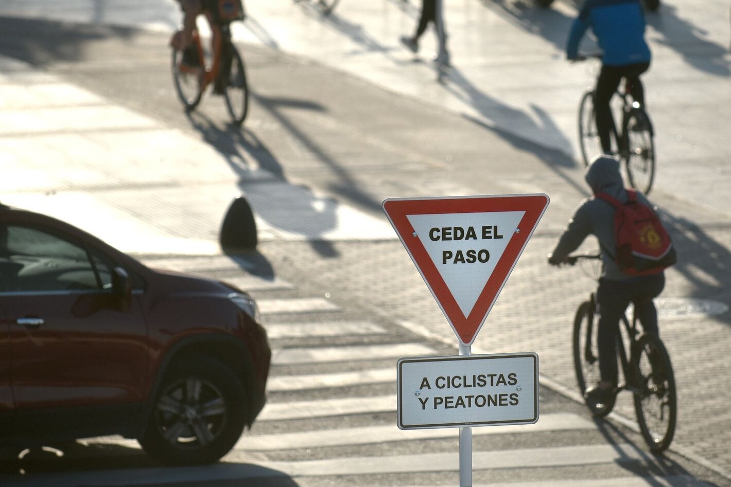 Foto de una calle con ciclistas, un cartel de ceda el paso y un auto esperando